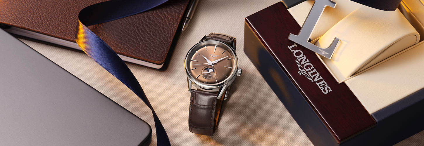 Eine elegante Uhr mit braunem Zifferblatt liegt neben einer Longines-Box und Lederwaren.