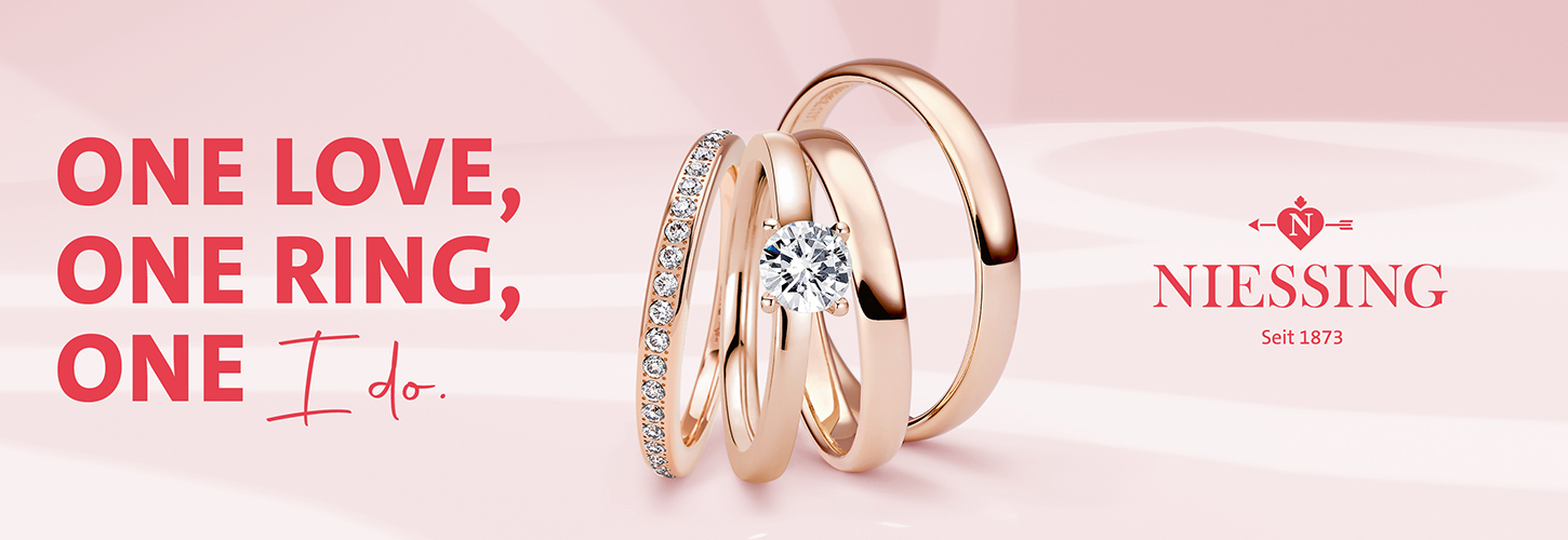 Drei goldene Ringe, einer mit Diamant, auf rosa Hintergrund mit "One Love, One Ring, One I do".