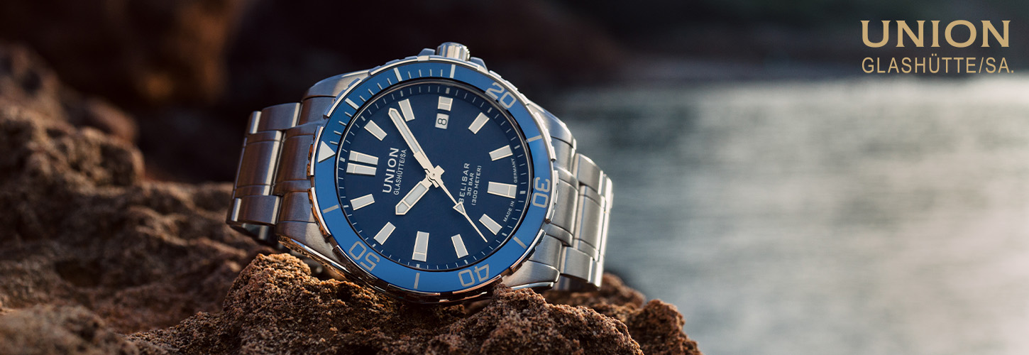 Eine elegante Armbanduhr mit blauem Zifferblatt und Edelstahlarmband auf einem Felsen.