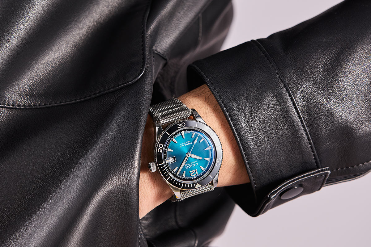 Eine Person trägt eine schwarze Lederjacke und eine Uhr mit blauem Zifferblatt.
