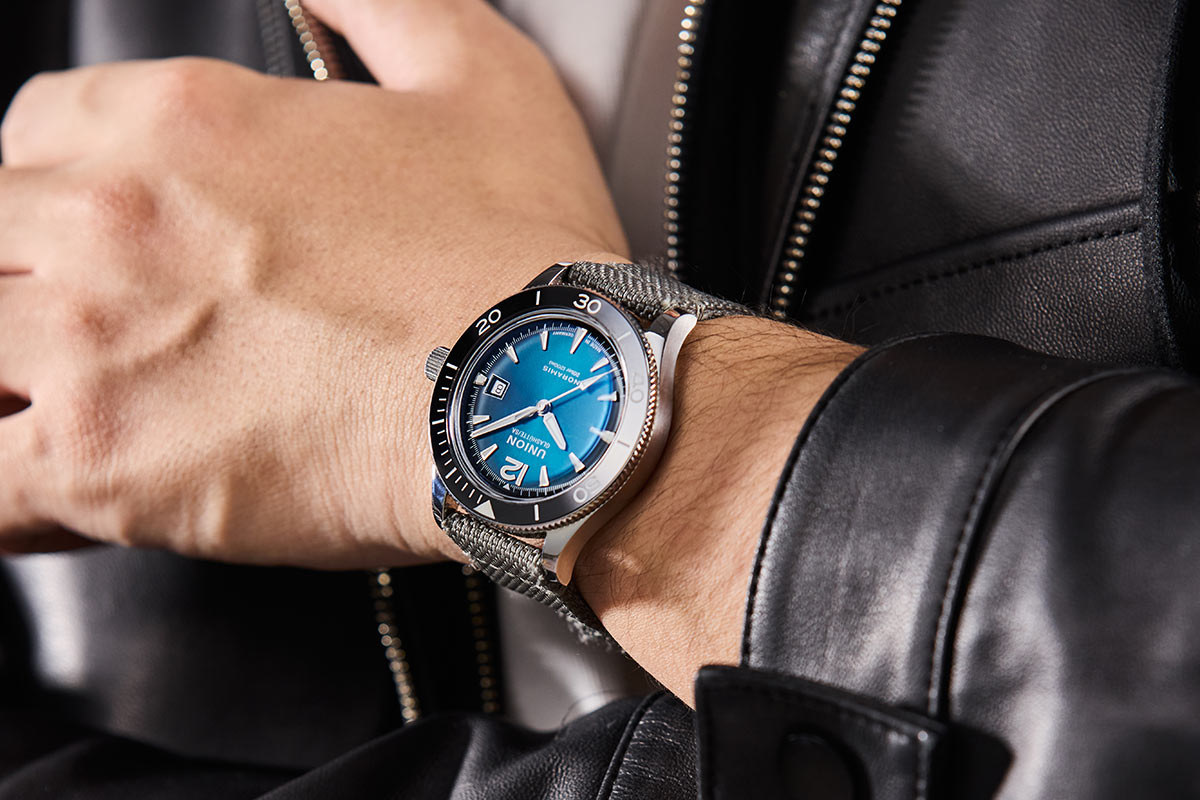 Person trägt eine schwarz-blaue Armbanduhr mit geflochtenem Band und Lederjacke.