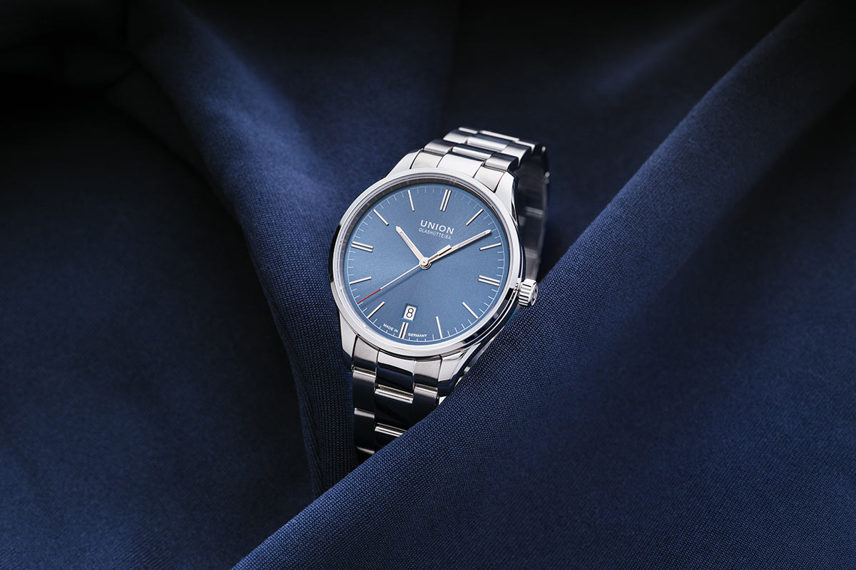 Eine elegante Armbanduhr mit blauem Zifferblatt auf einem dunkelblauen Tuch.