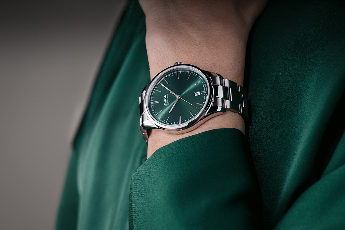 Eine Person trägt eine elegante silberne Uhr mit grünem Zifferblatt.