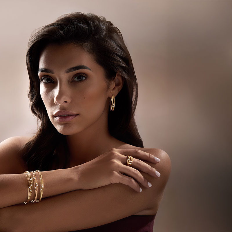 Junge Frau mit langen dunklen Haaren schaut ruhig, trägt goldenen Schmuck