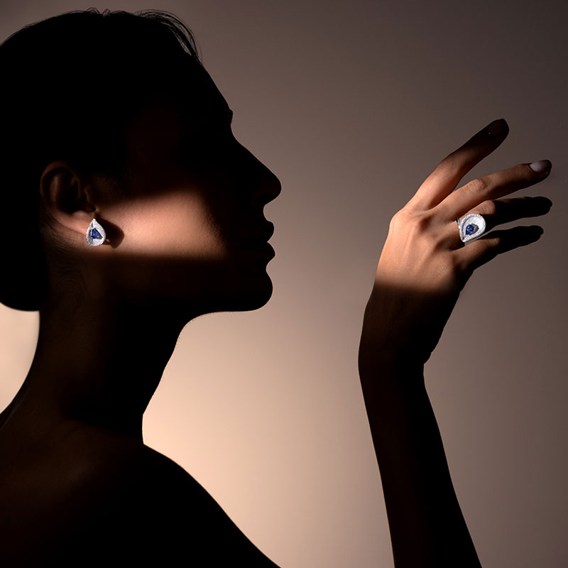 Eine Frau im Profil mit nachdenklichem Ausdruck trägt funkelnden blauen Schmuck