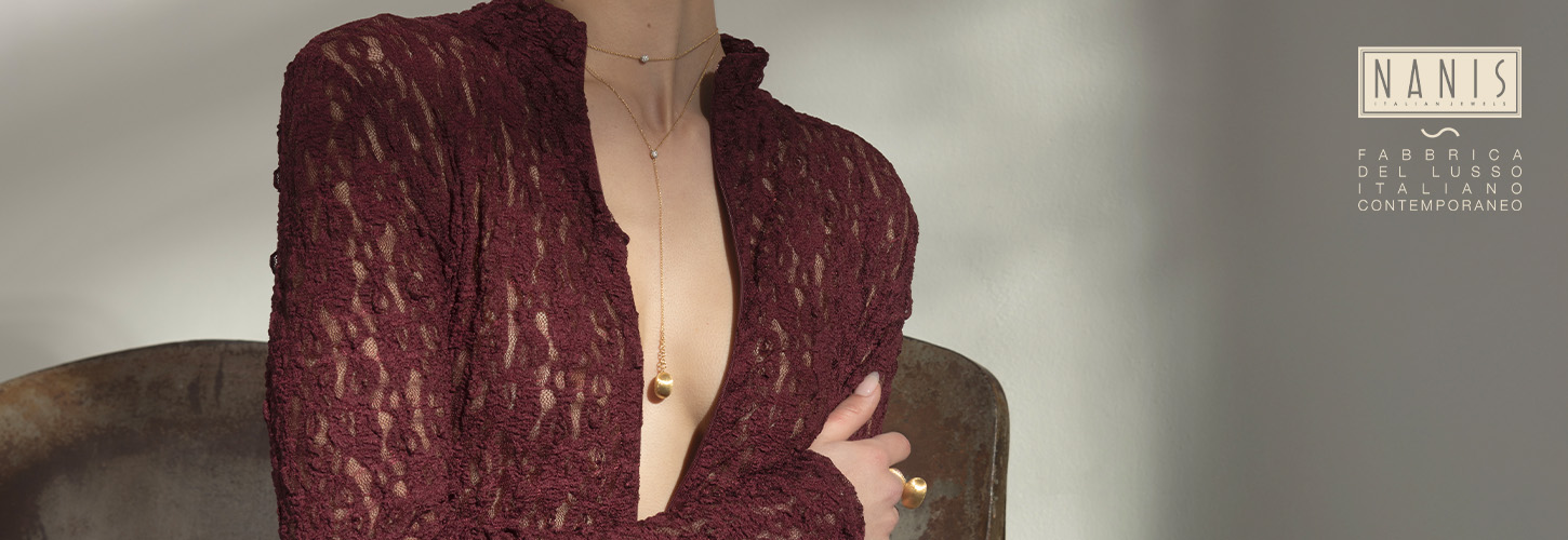 Eine Frau mit beigem Teint trägt ein weinrotes Spitzenkleid und goldenen Schmuck