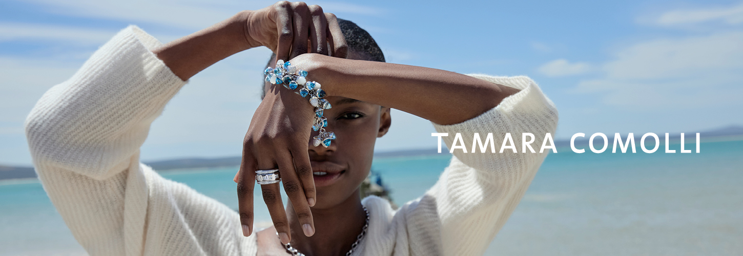 Eine junge Person mit entspannter Miene trägt silbernen Schmuck und steht am Meer