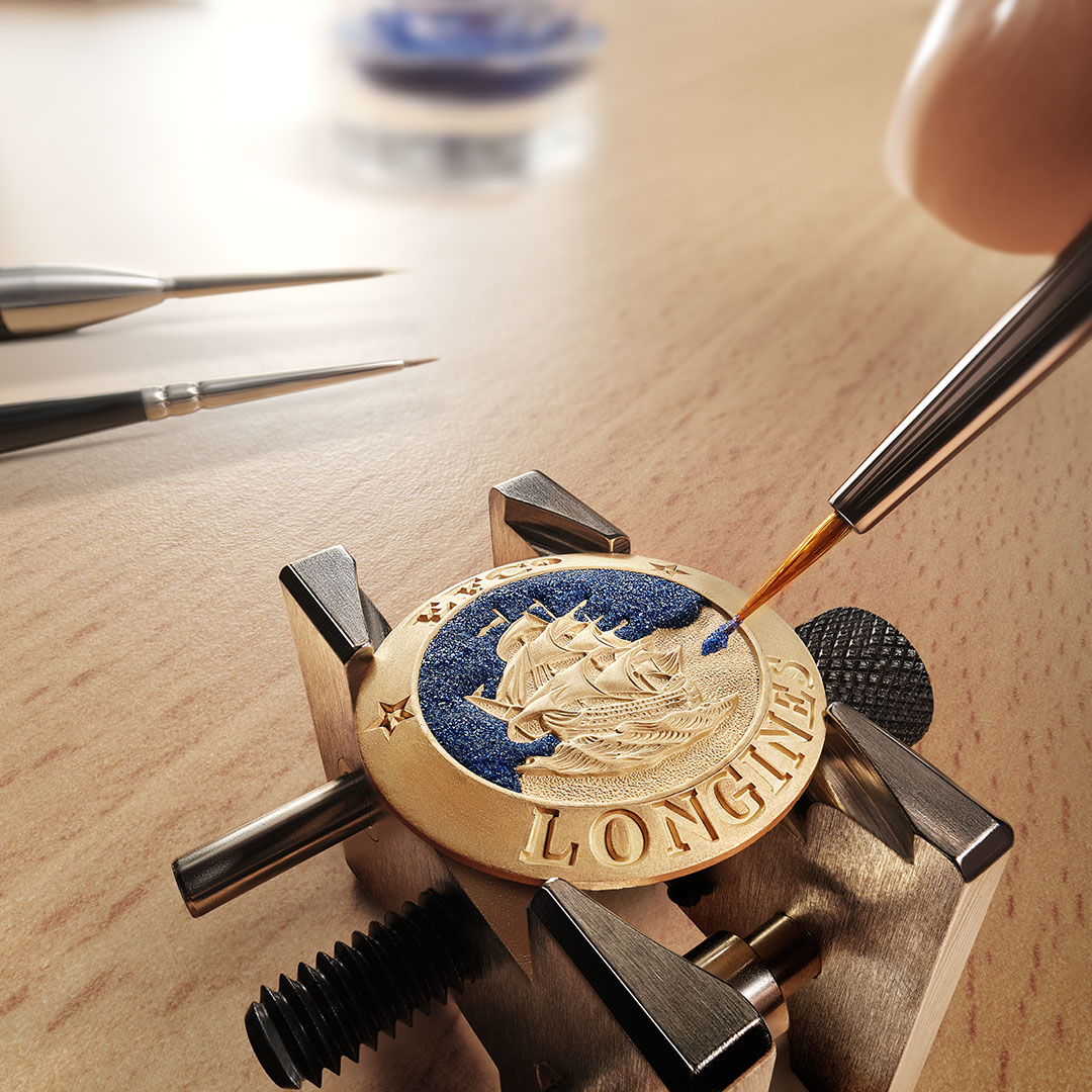 Eine Hand bemalt ein goldfarbenes Medaillon mit einem Reliefschiff auf blauem Hintergrund