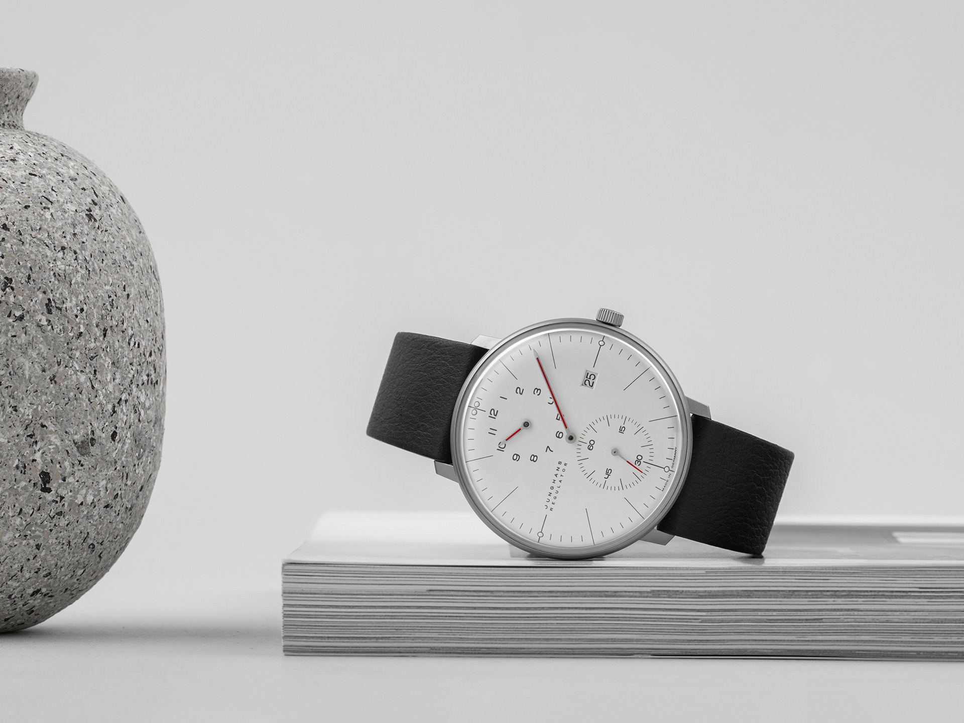 Eine elegante Uhr mit weißem Zifferblatt und schwarzem Lederarmband liegt auf Zeitschriften