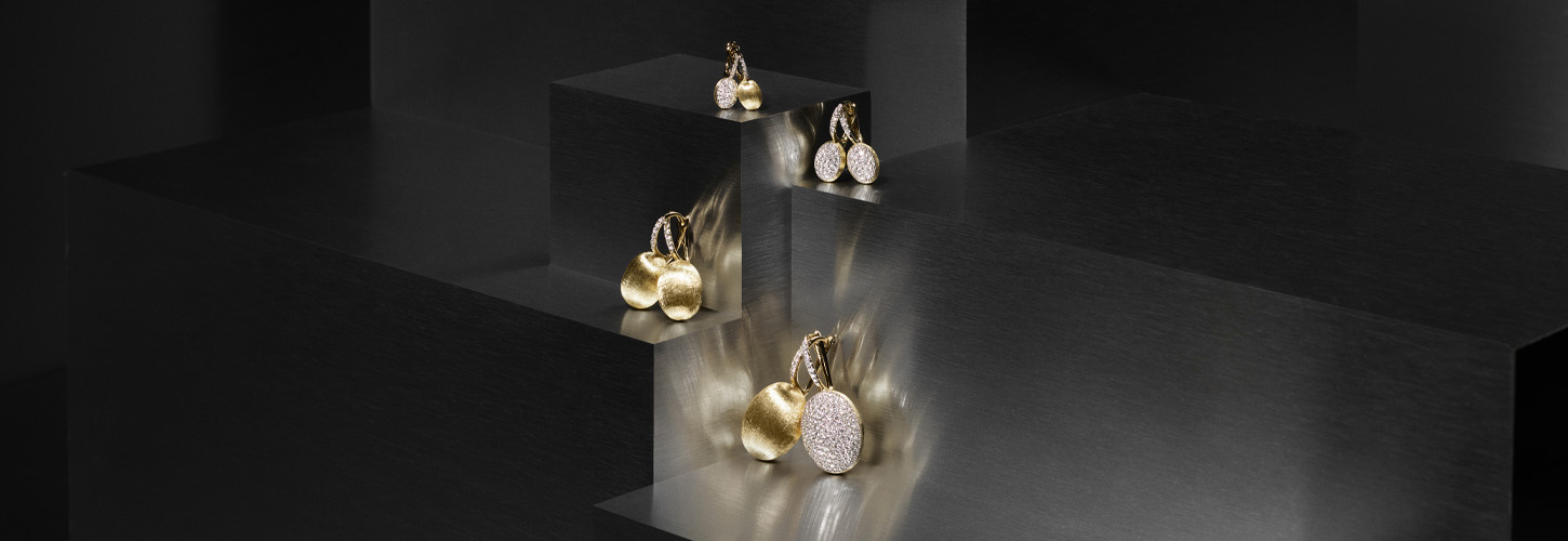 Glänzende runde Ohrringe in Gold und Silber auf schwarzen Stufen mit Spiegelungen