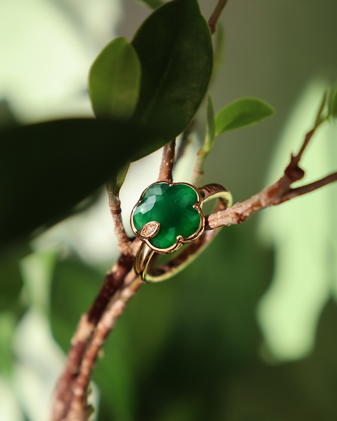 Ein goldener Ring mit grünem, blütenförmigem Edelstein sitzt auf einem Zweig