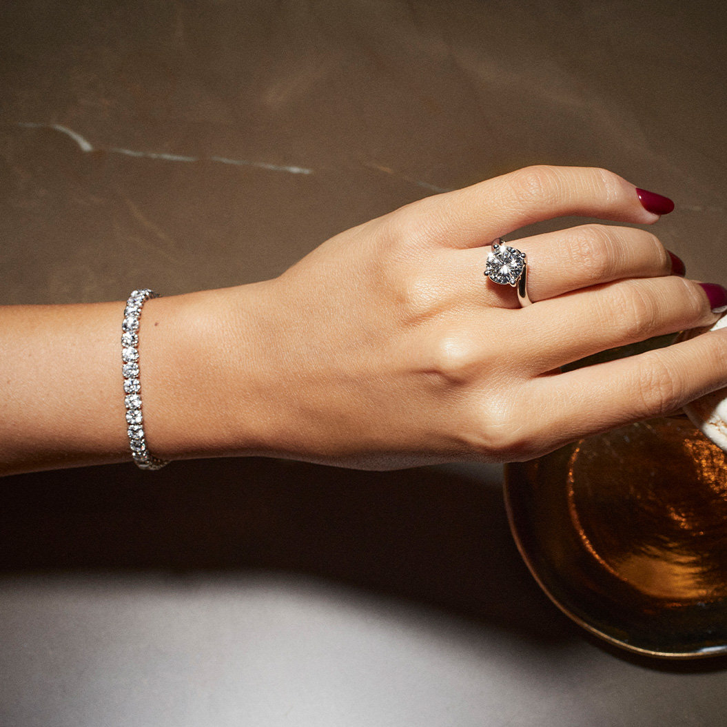 Eine gepflegte Hand mit rotem Nagellack trägt einen funkelnden Diamantring und ein Tennisarmband