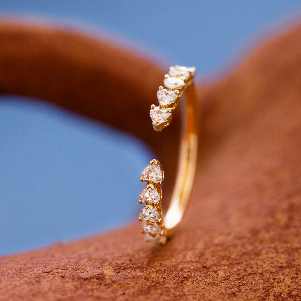 Ein goldener Ring mit kleinen funkelnden Diamanten liegt auf einer braunen Oberfläche