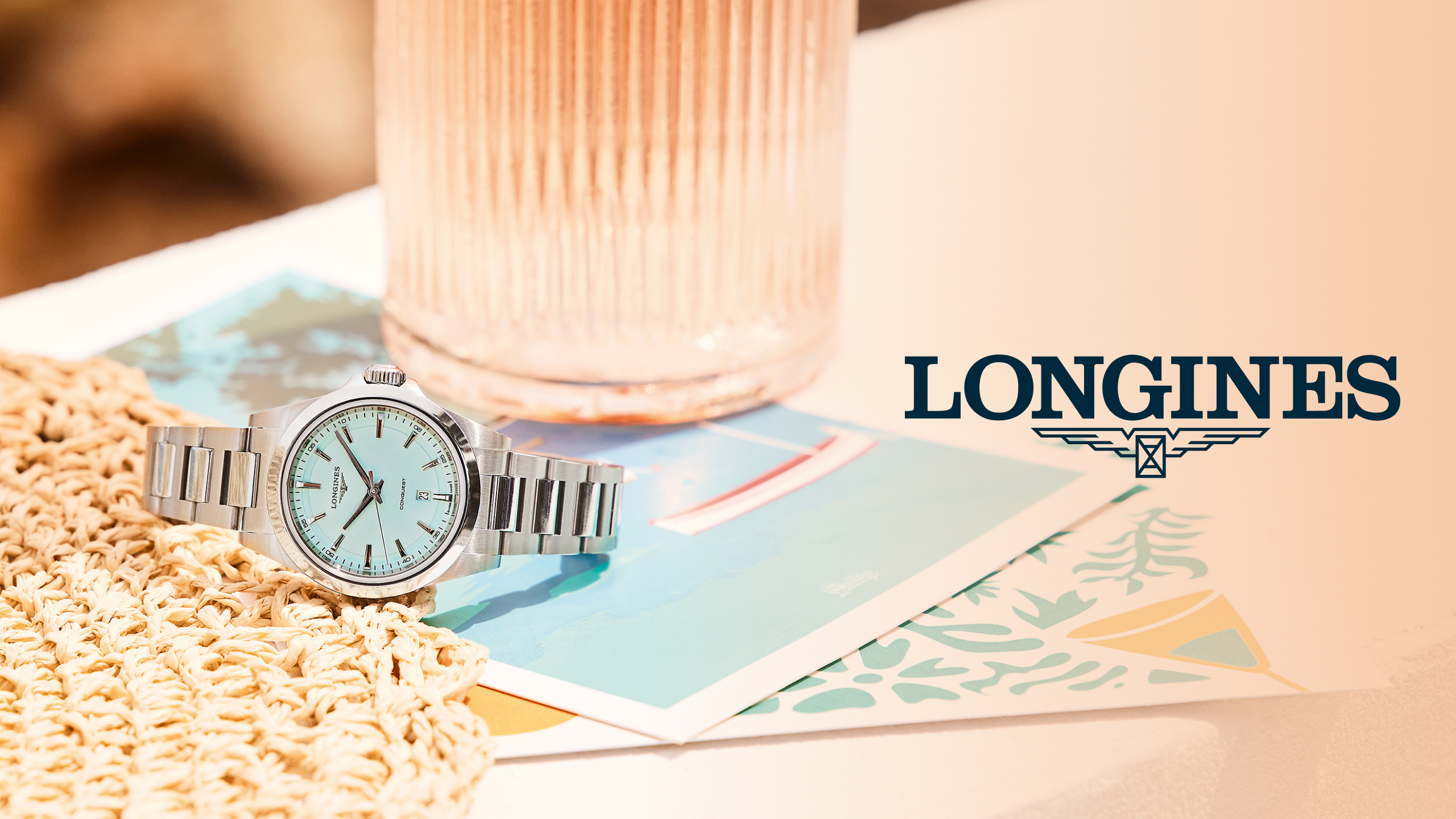 Silberne Armbanduhr mit hellblauem Zifferblatt neben rosa Glas und Longines Logo